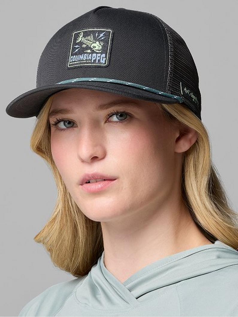 Woman wearing a dark gray trucker hat with mesh back panels and a square logo patch on the front.