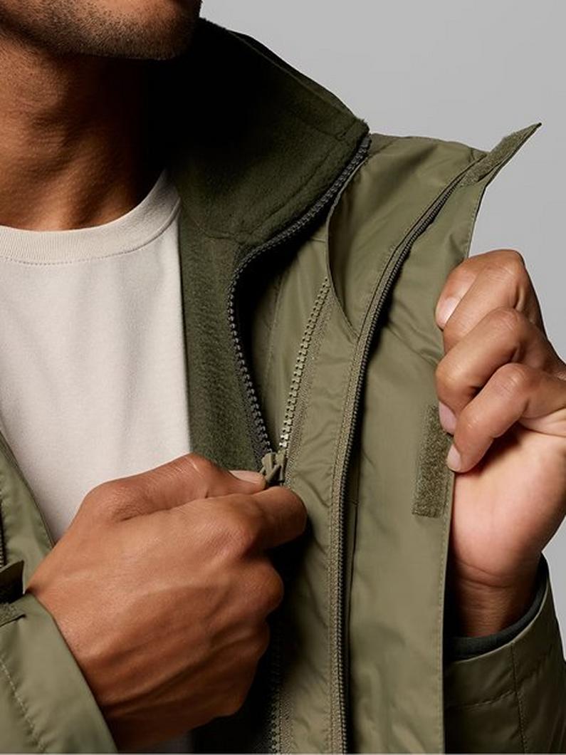 Person wearing white t-shirt holding open an olive green zip-up jacket with layered collar design.