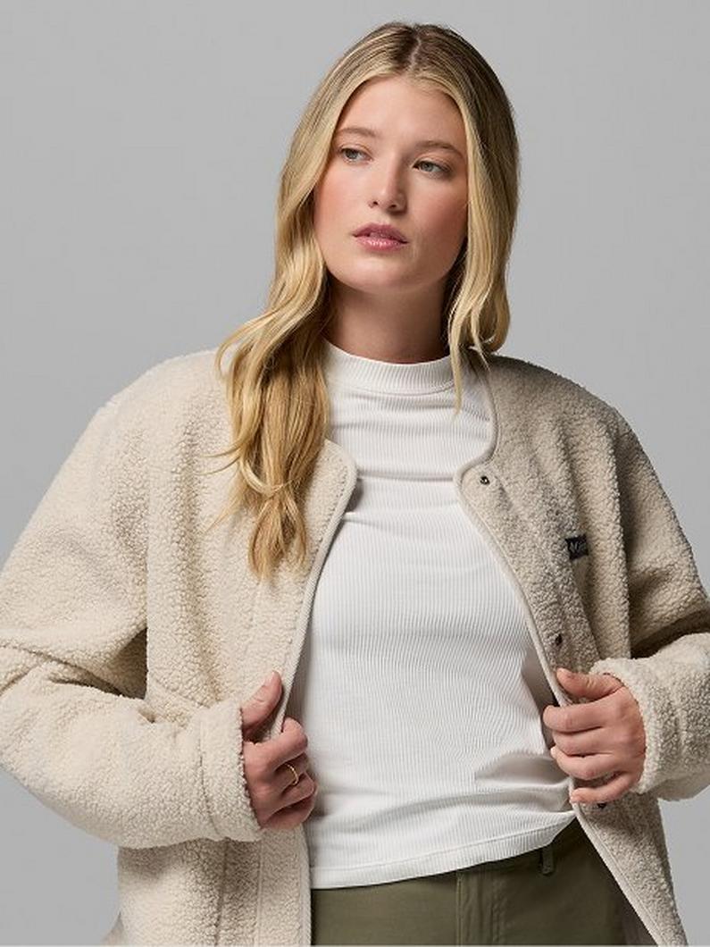 Woman wearing white turtleneck sweater and beige fleece jacket over olive pants.