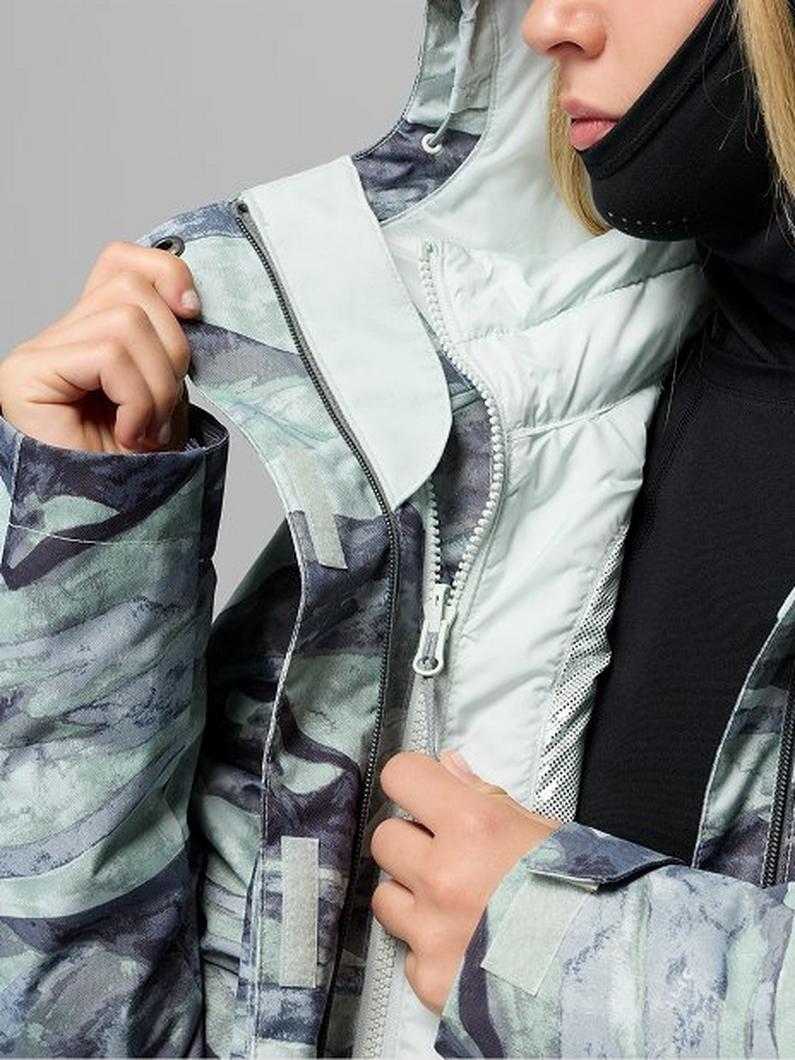 Woman wearing a puffer vest with camouflage print sleeves and white front panel with zipper closure.