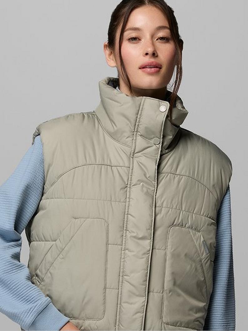 Woman wearing a sage green quilted puffer vest with high collar over a light blue long-sleeve top.