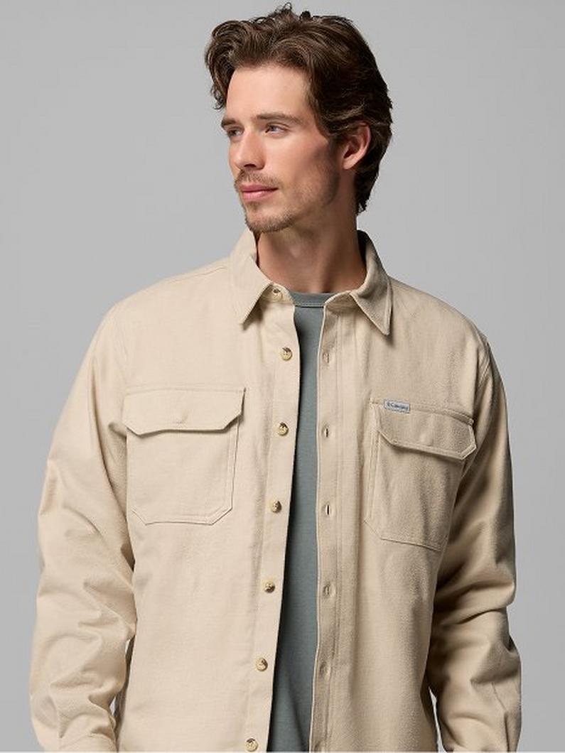 Man wearing an unbuttoned beige shirt jacket with chest pockets over a gray t-shirt, looking to the side.