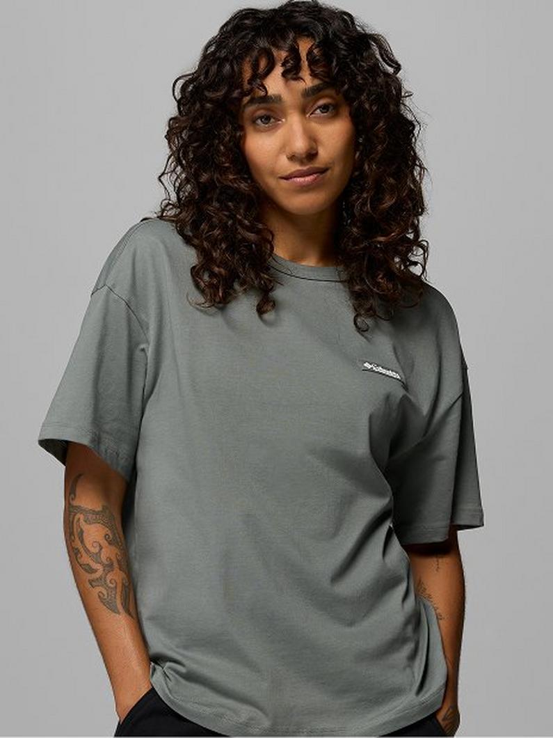 Woman with curly hair wearing an oversized sage green short-sleeve t-shirt with chest logo.