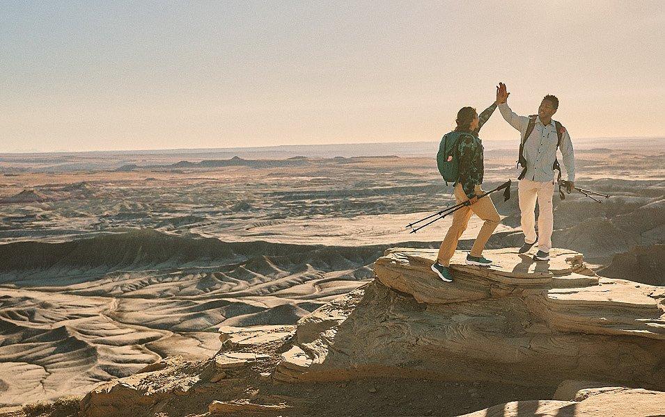 Two hikers at the top of a rocky hill overlooking a desert.