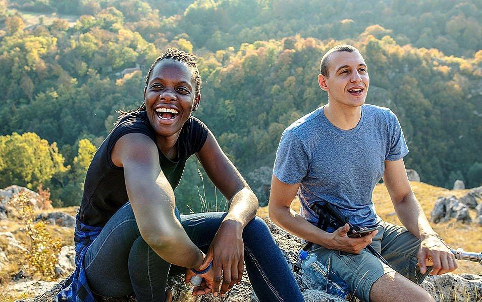 Two people sitting on rocks at the top of a hill smiling.