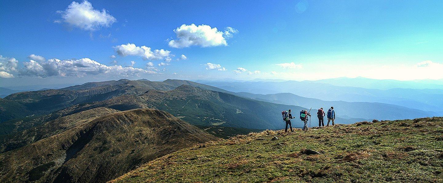 A beautiful image depicting four backpackers hiking over a scenic mountain landscape. 