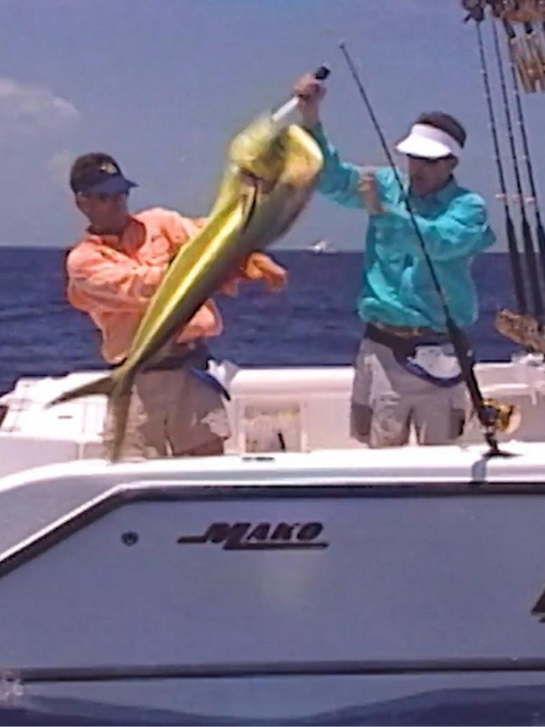 Two anglers on a boat holding up a large mahi-mahi fish they caught while deep sea fishing.