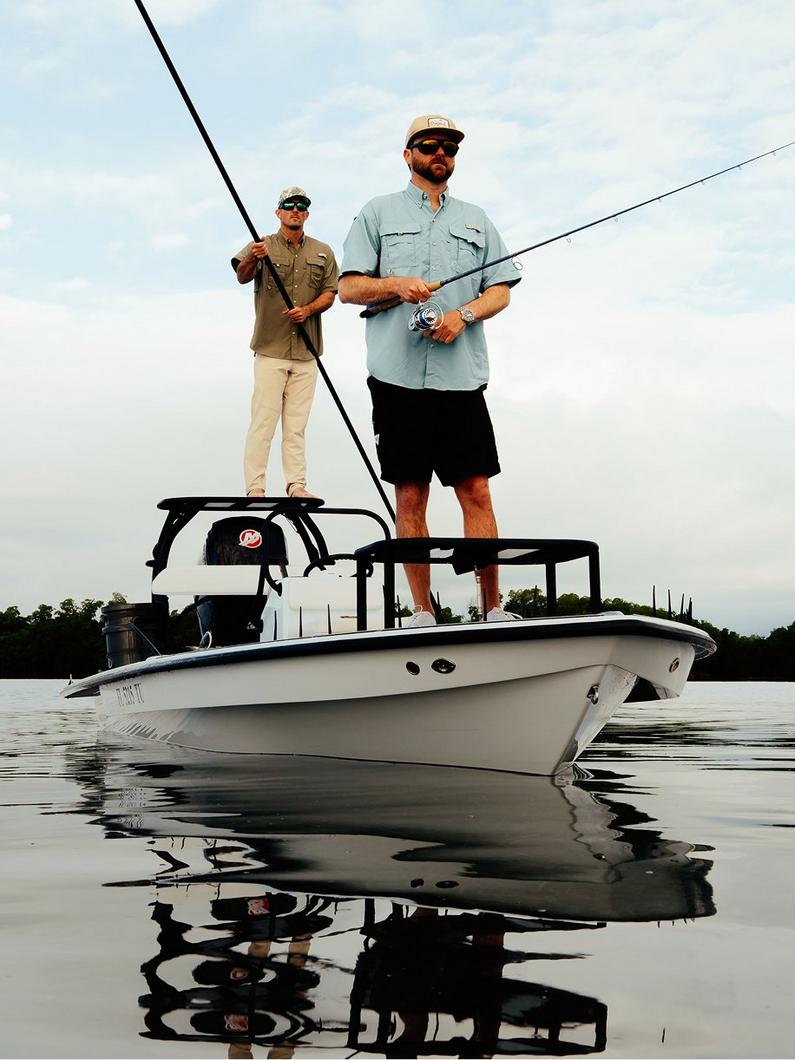 Two men fishing from an elevated platform on a white boat in calm waters.