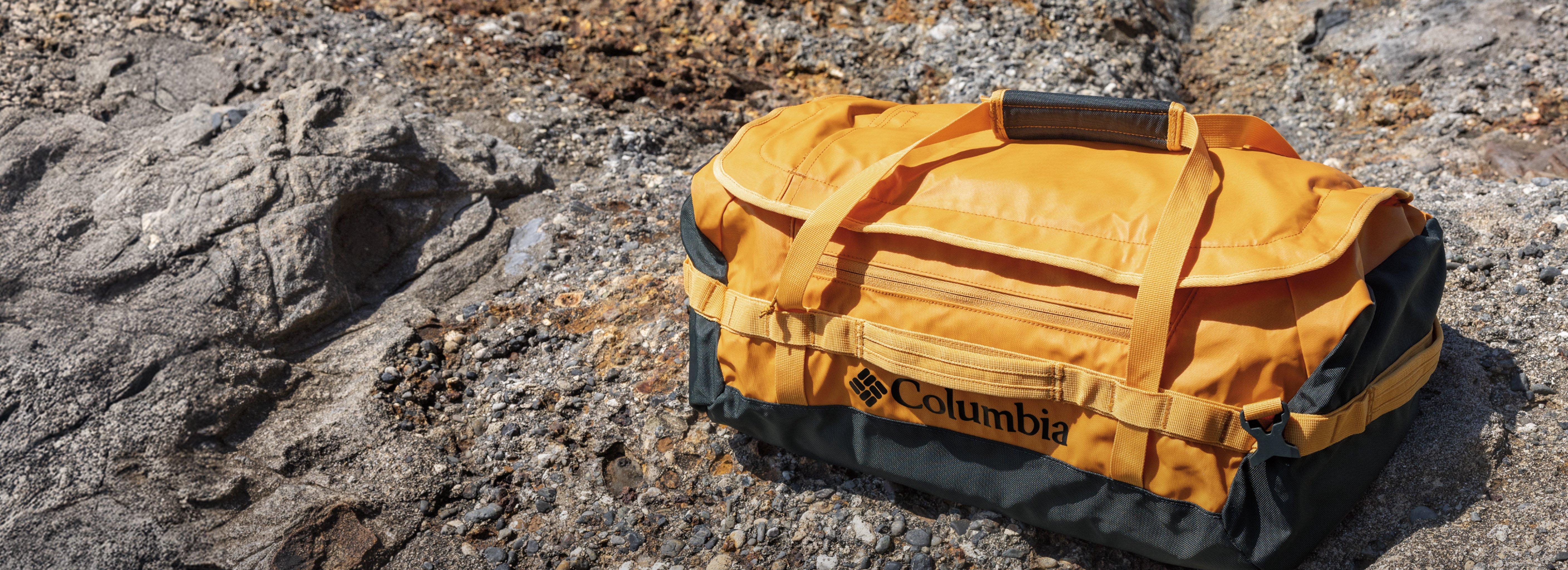 Yellow and black duffel bag with multiple straps and zippered pockets resting on rocky terrain.