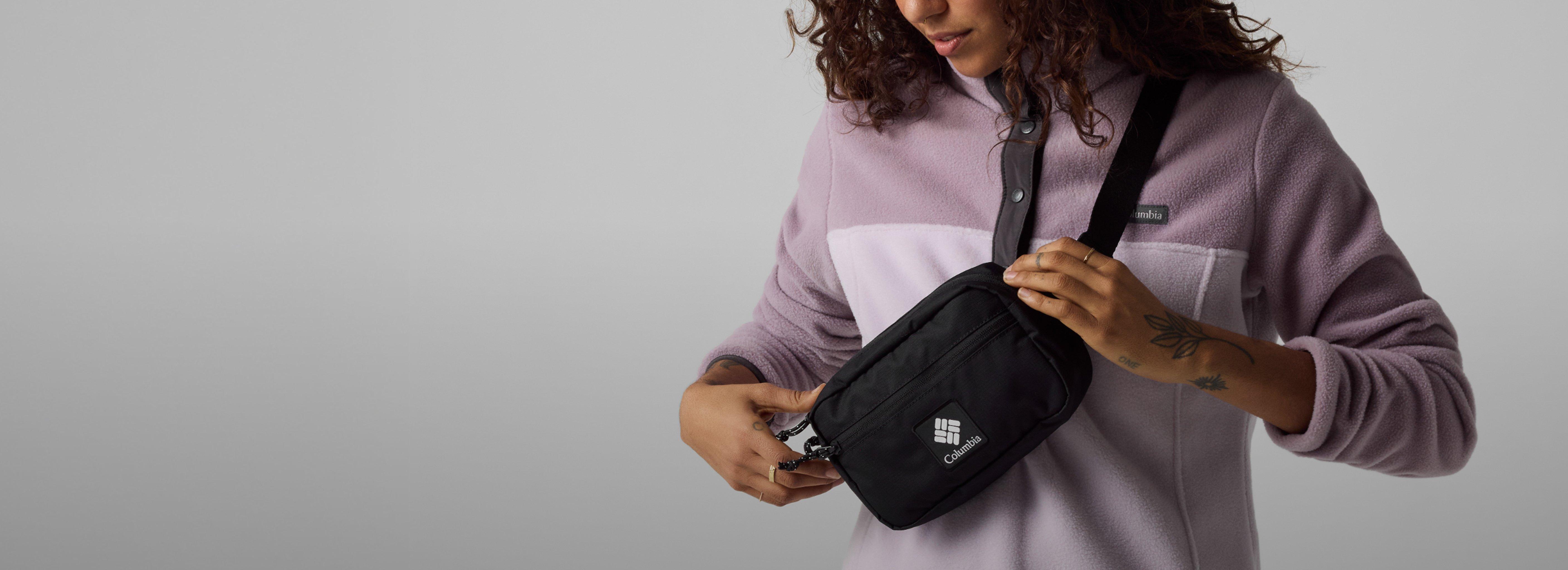 Woman wearing purple fleece pullover opening black crossbody bag worn across her chest.