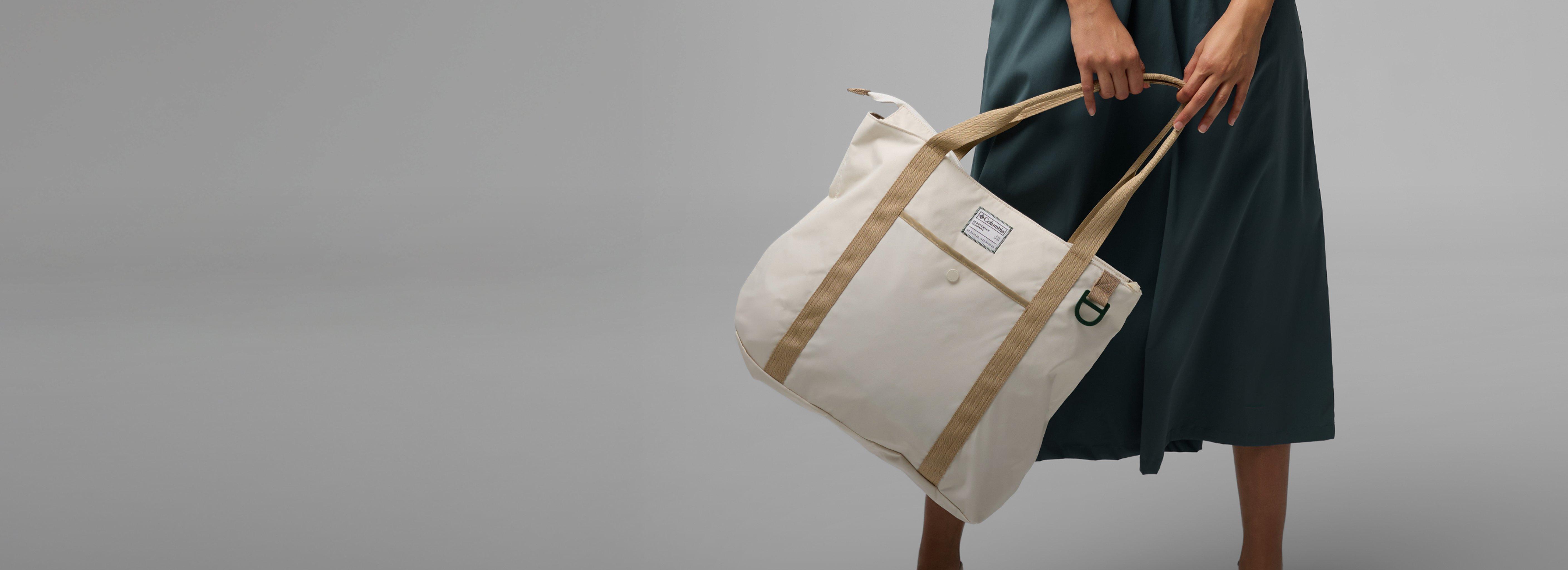 Person wearing green dress holding cream canvas tote bag with tan straps and small label patch.