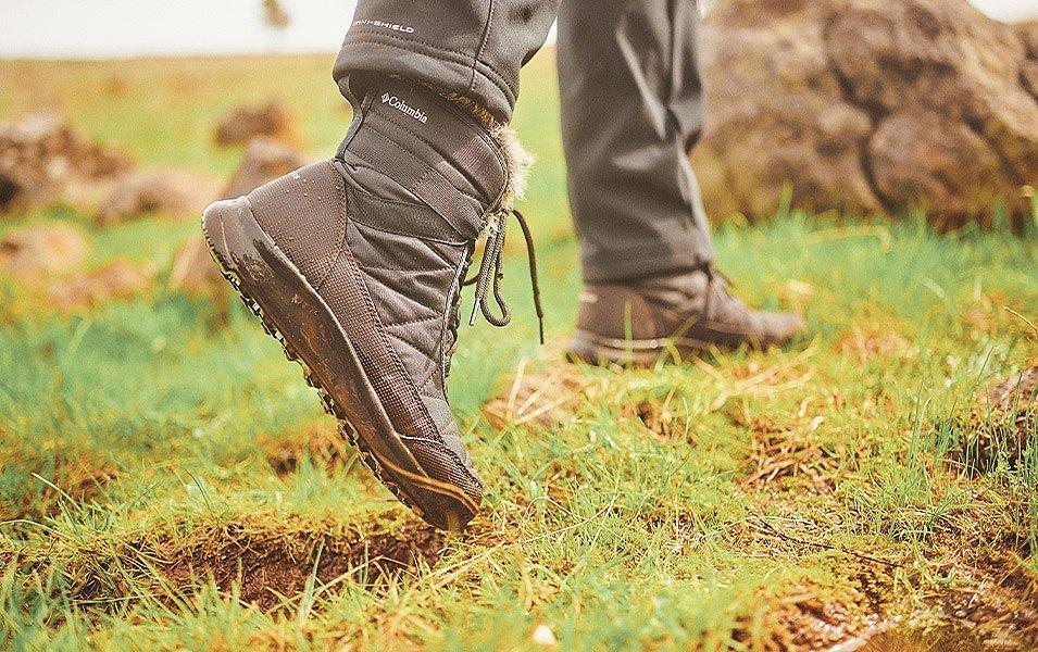 A person in Columbia Sportswear waterproof boots walking across a wet and muddy field. 