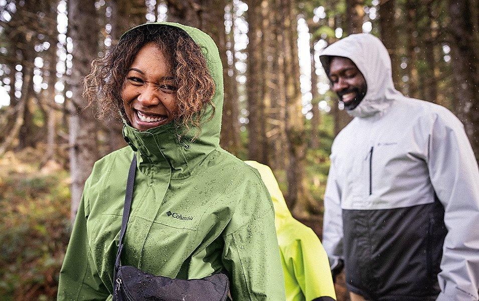 A man, woman, and child all in Columbia Sportswear Rain jackets hike through a forest in the rain.  