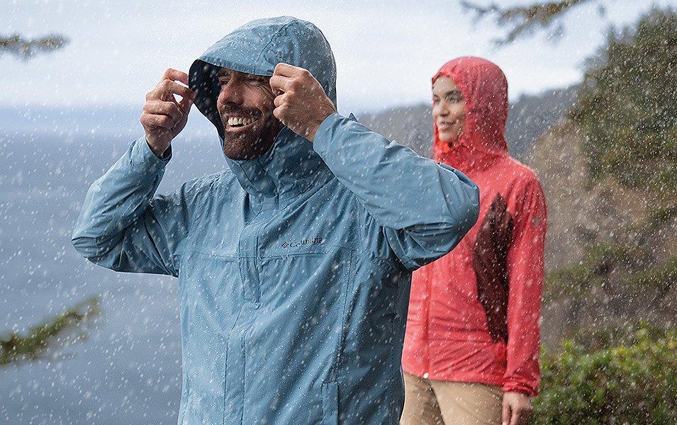 Two people in Columbia Sportswear rain jackets stand on a hillside in the rain. 