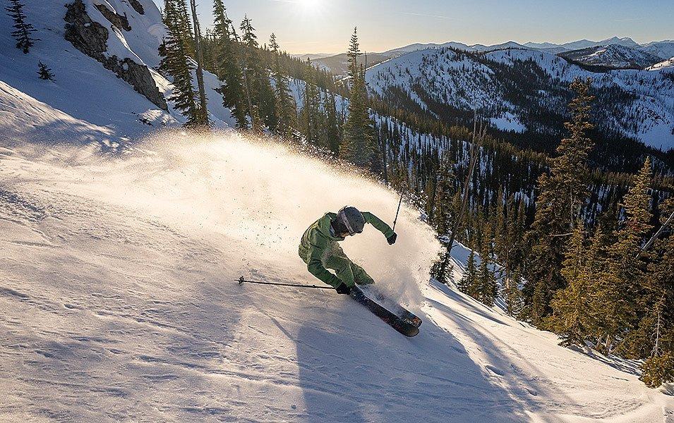A skier rides down a mountain in a green Columbia Sportswear ski snow set.  