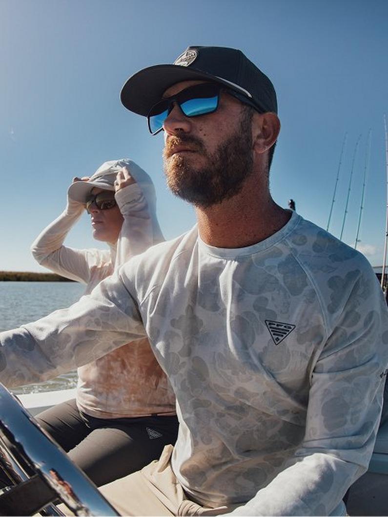 Man wearing blue sunglasses and black cap in long-sleeve shirt while boating on the water.