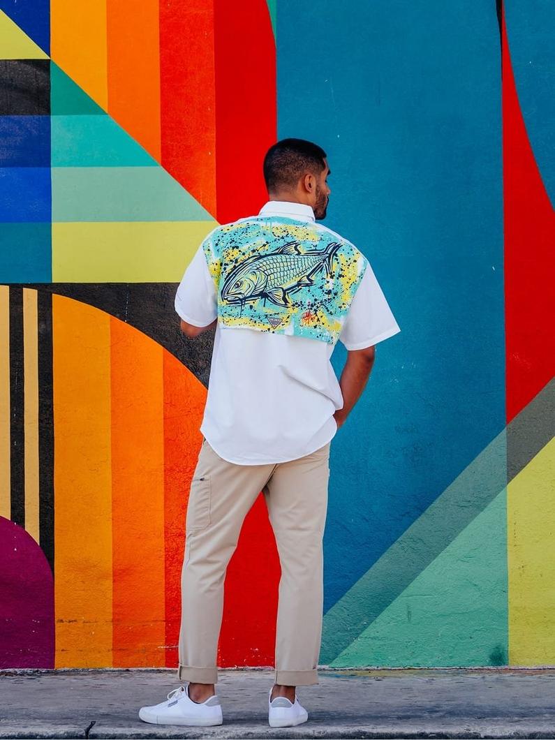 Man wearing white short-sleeve shirt with colorful fish graphic on back and beige pants.