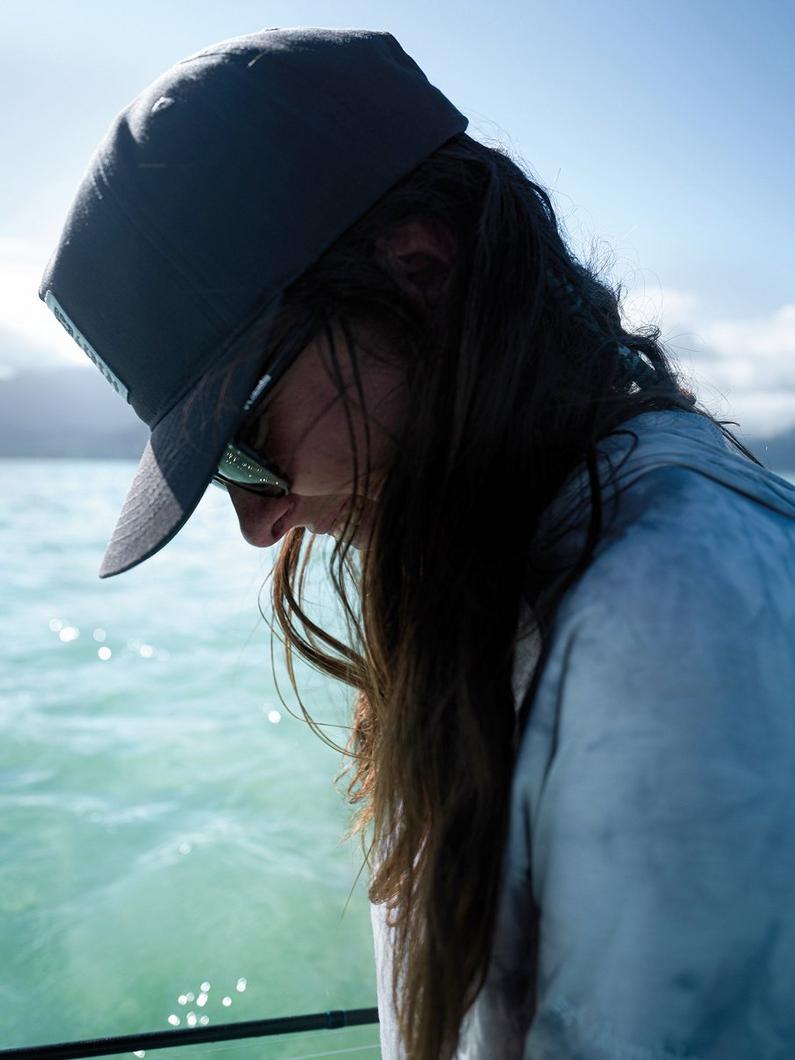 Woman wearing dark bucket hat and sunglasses looking down while on a boat over turquoise water.