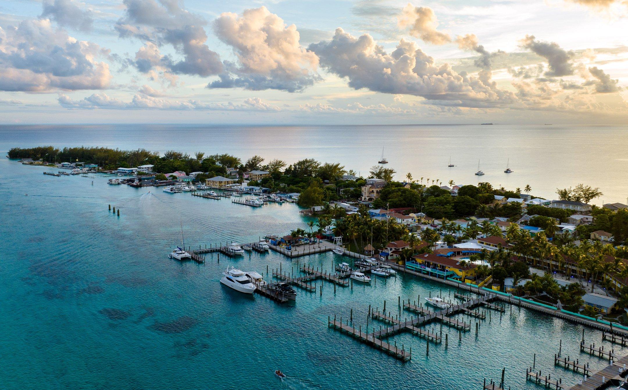 Aerial view of a tropical coastal marina with boats docked at wooden piers and residential buildings.