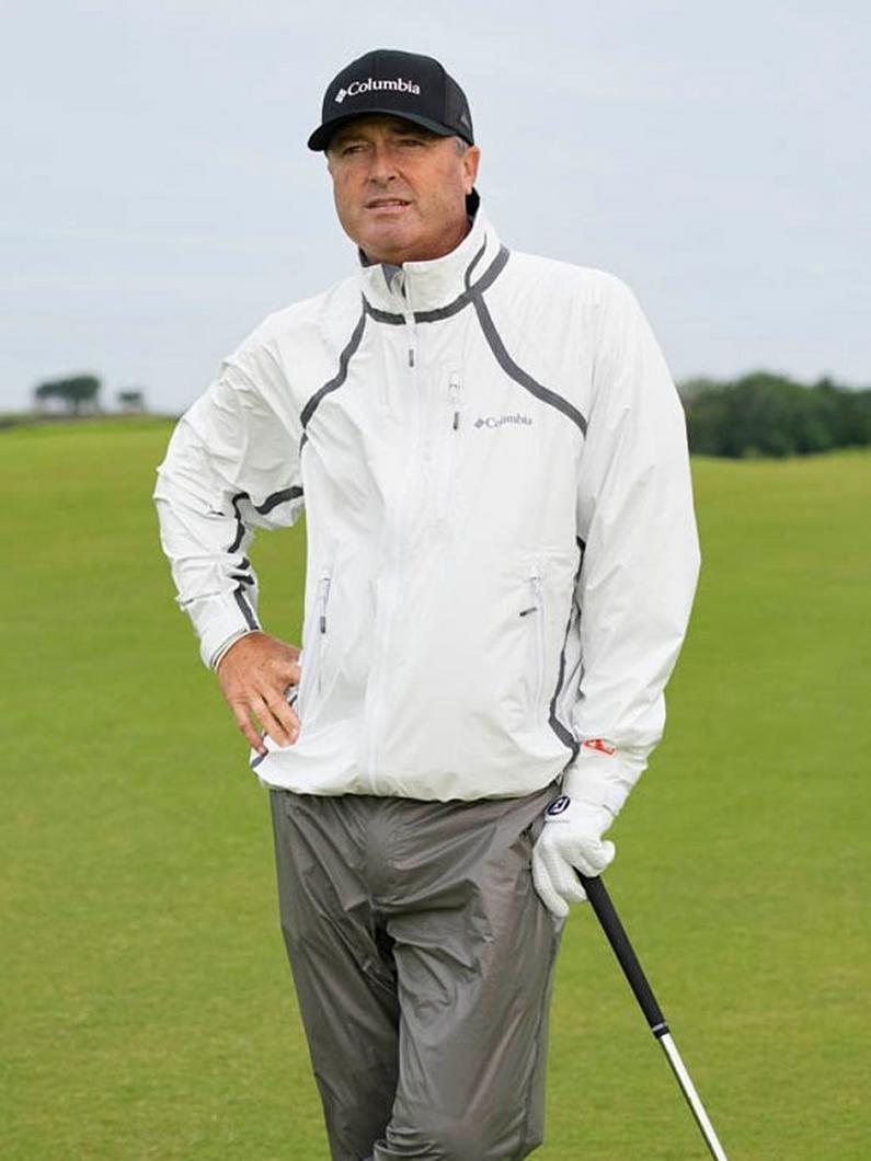 Man wearing white quarter-zip pullover jacket with gray trim and black cap while standing on golf course.