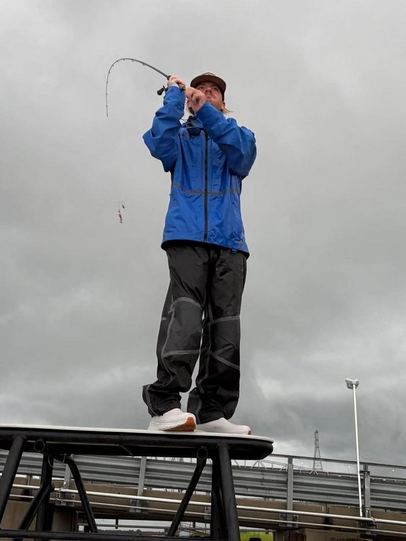Person wearing blue jacket and dark pants standing on platform holding bent fishing rod.