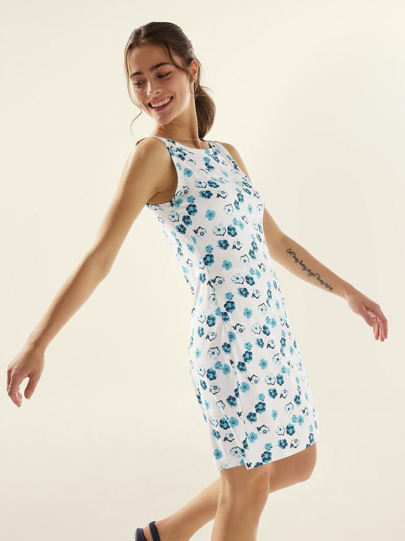 Woman smiling and posing in a white sleeveless dress with blue floral print.