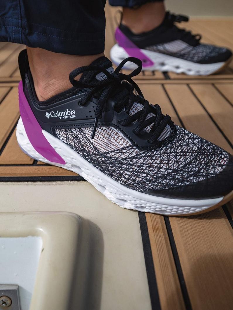 Athletic shoe with black and white mesh upper, purple midsole accent, and white sole on wooden deck.