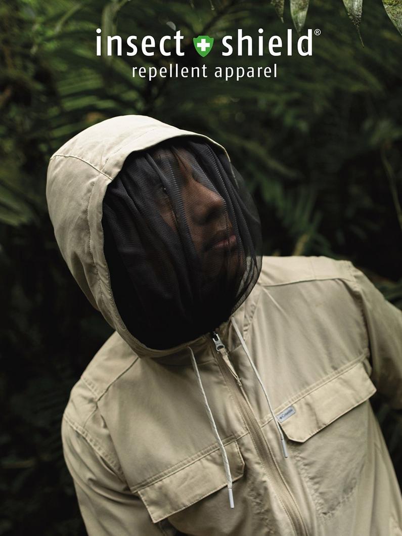 A man wearing a tan long sleeve shirt with a hood up and face net covering over their face as they stand in the jungle with text: Insect Shield® repellent apparel