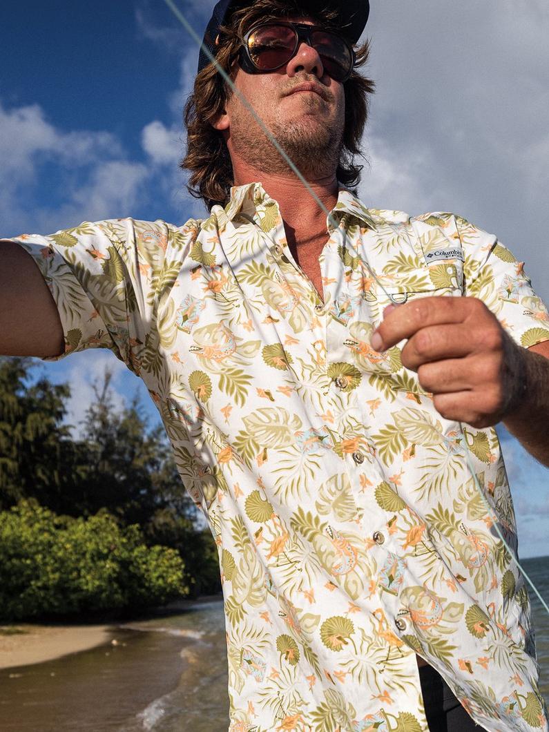 Man wearing tropical print shirt and sunglasses holding fishing line outdoors.