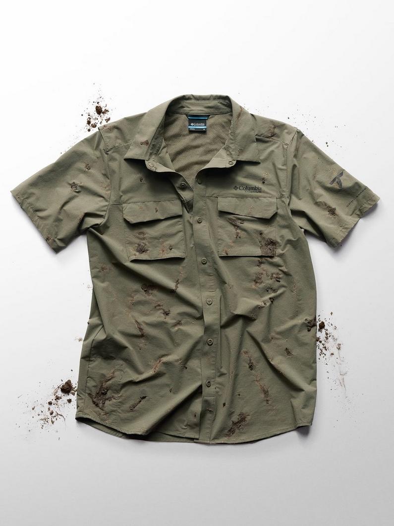 Olive green short-sleeve fishing shirt with chest pockets and mud stains throughout.