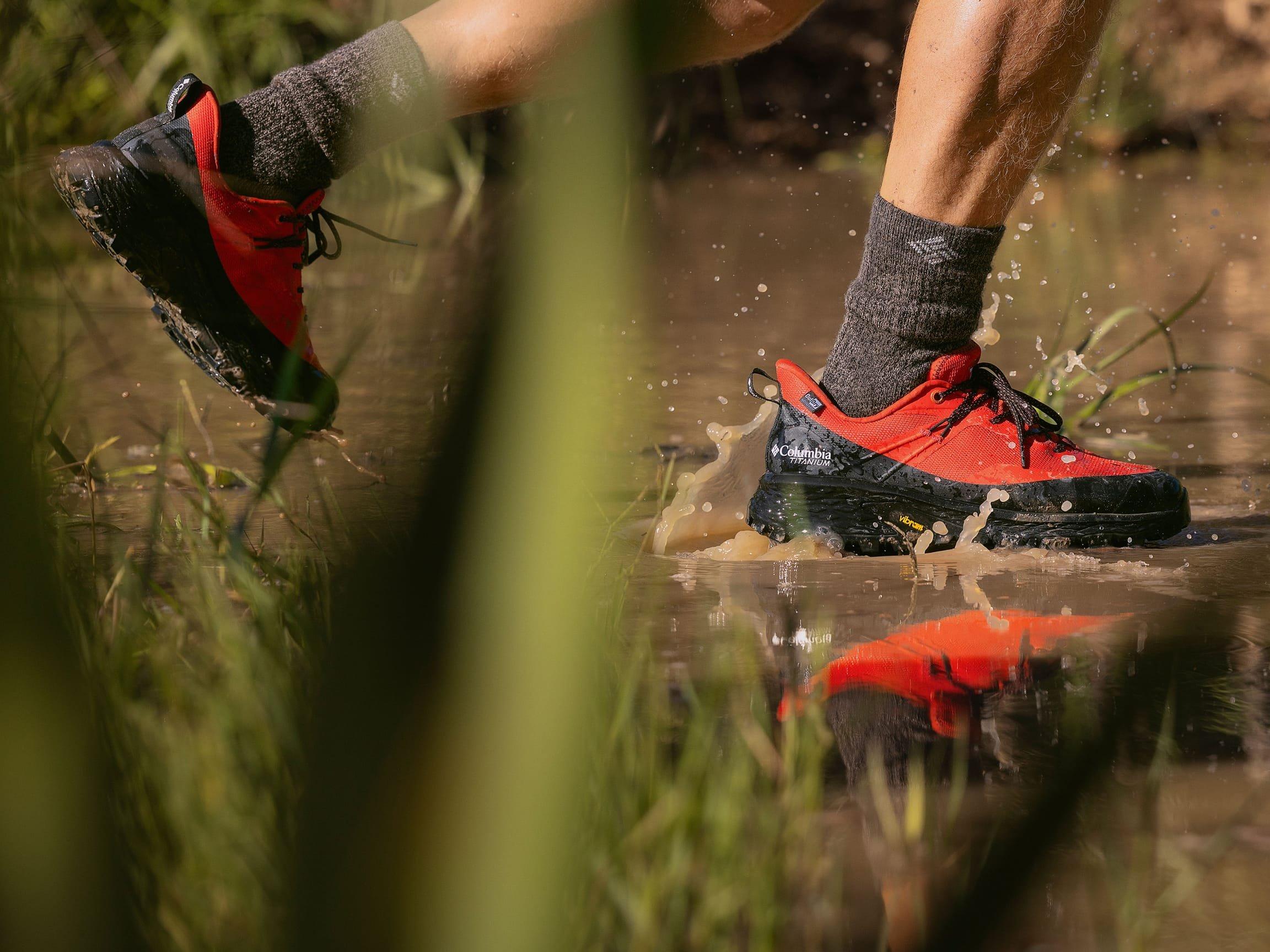 Person running through muddy water wearing red and black waterproof hiking shoes with gray socks.