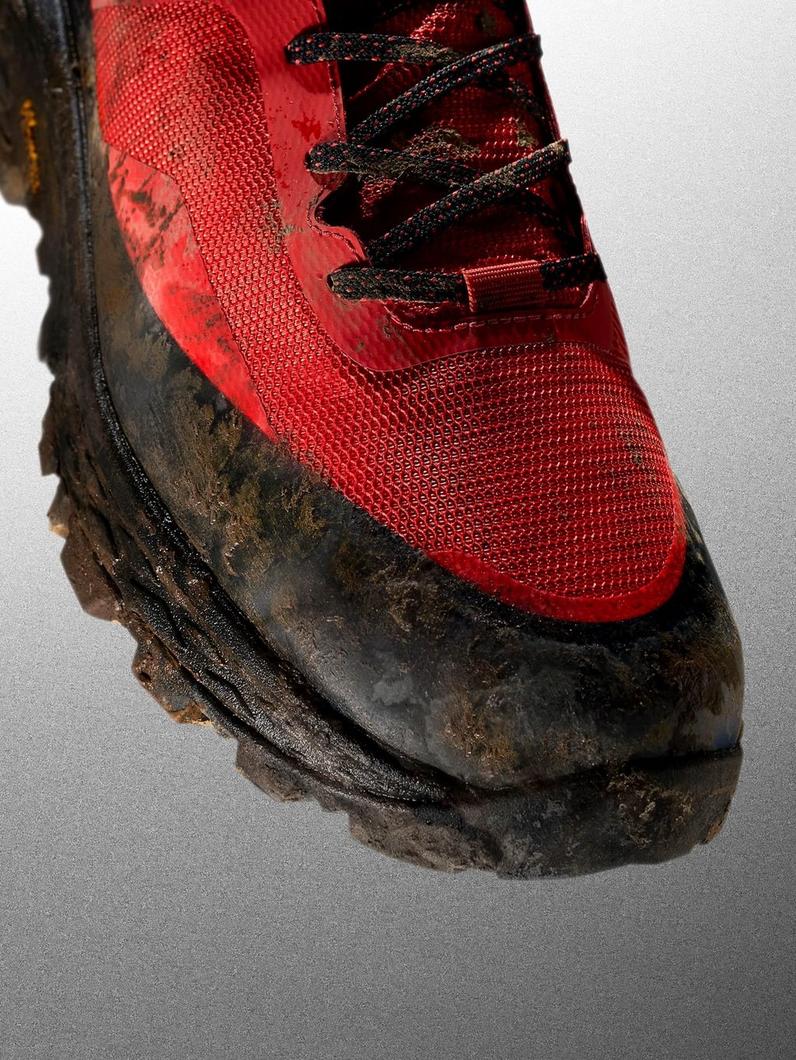 Red hiking boot with black laces and muddy black rubber sole.