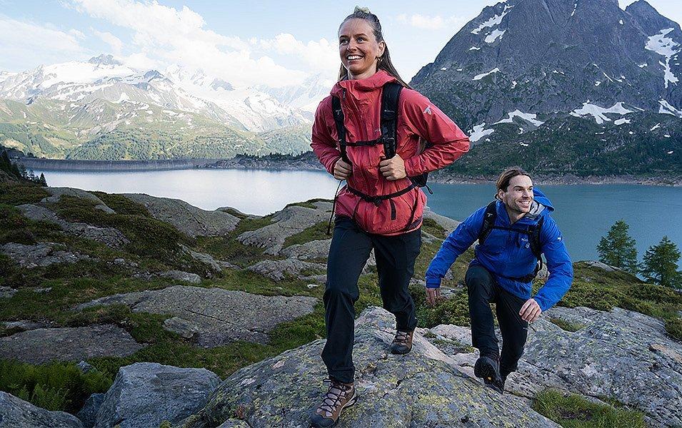 Two hikers happily walk up a rocky trail enroute to another summit. 