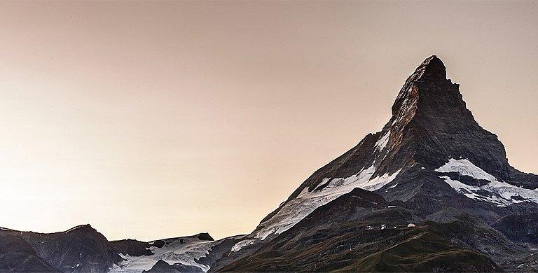 Dramatic photo of steep, pyramid-like peak with glacier field below. 