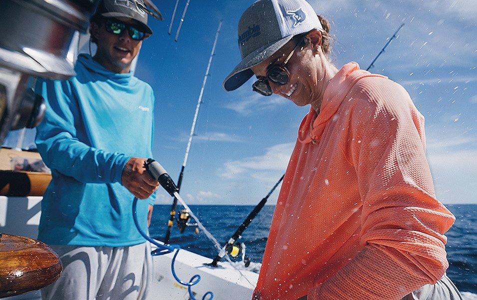 A man and a woman wearing Columbia Sportswear PFG sun protective shirts on a fishing boat in the ocean.   
