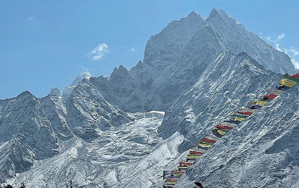 Prayer flags fly in the foreground, with the majestic peak looming in the distance. 