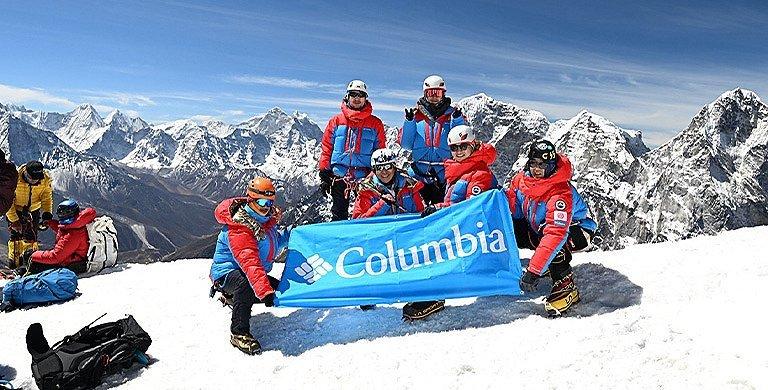 Six mountain climbers, all wearing Columbia Sportswear's apparel, raise a Columbia banner on the summit of Mt. Lobuche while training for Mt. Everest. 