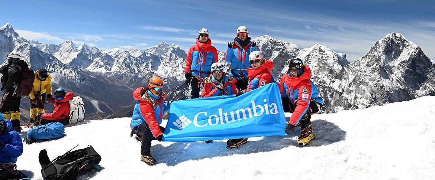 Six mountain climbers, all wearing Columbia Sportswear's apparel, raise a Columbia banner on the summit of Mt. Lobuche while training for Mt. Everest. 