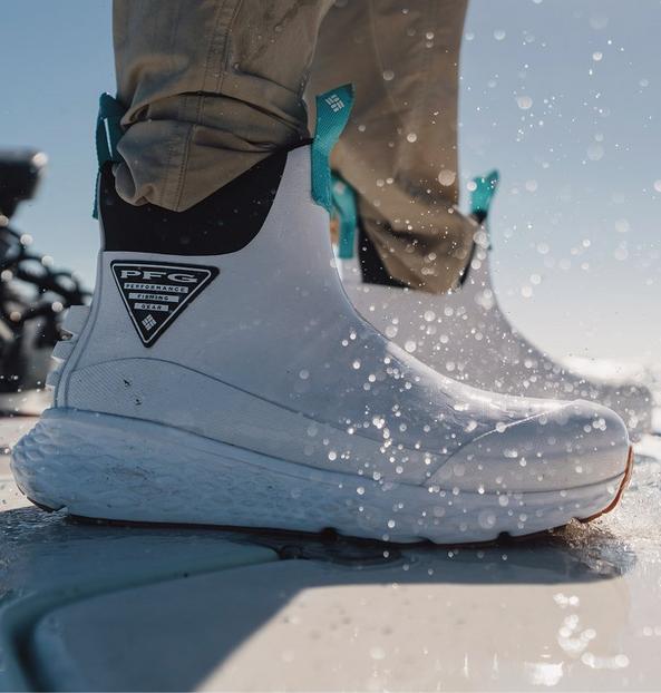 Person wearing white waterproof boots with teal pull tabs walking through water with splashes around them.