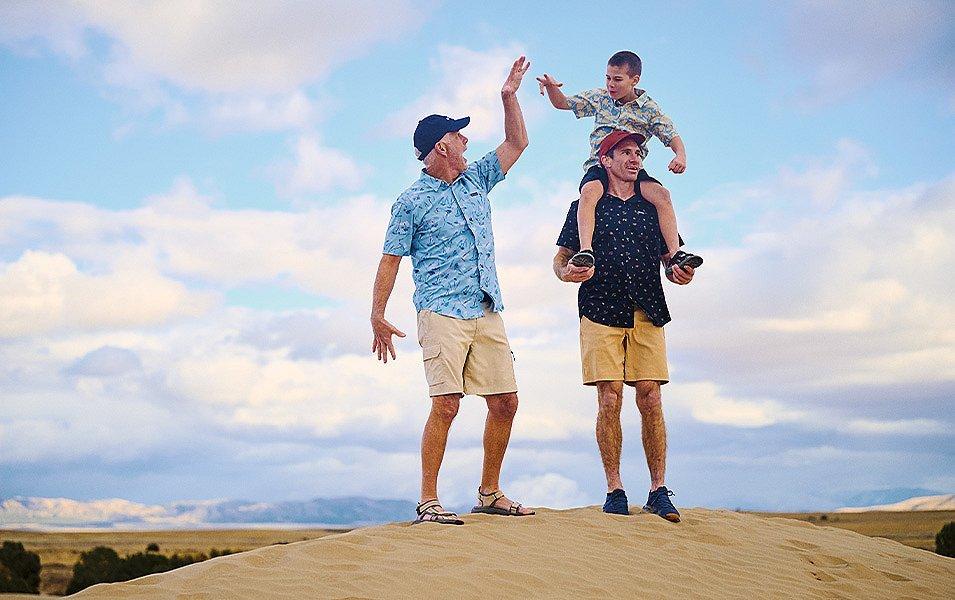 Two men, one hoisting a boy on his shoulders, stand a top a sand dune.