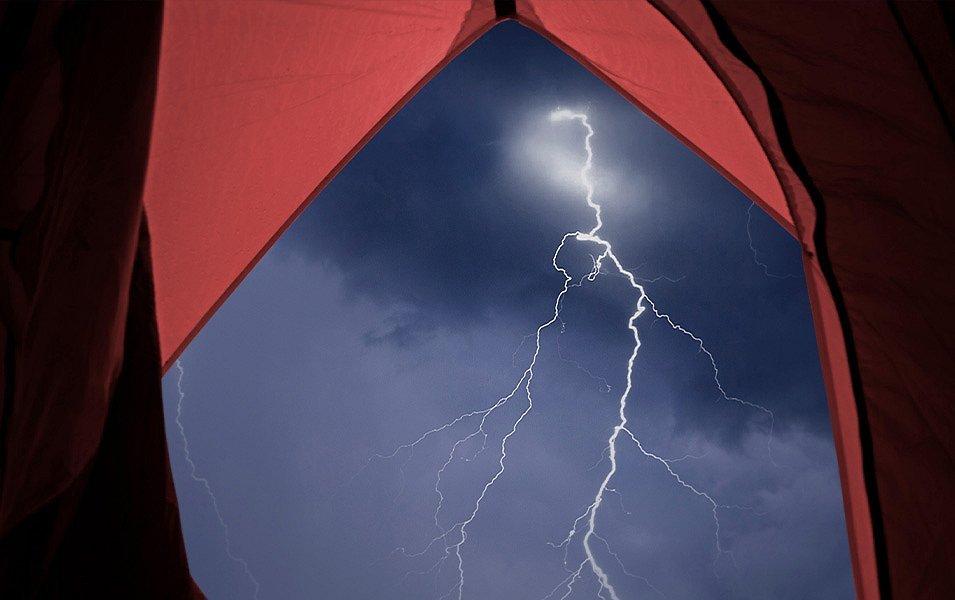 From inside a tent, you can see out of the front vestibule to the night sky. The sky is dark, and a brilliant bolt of lightning strikes the ground. 