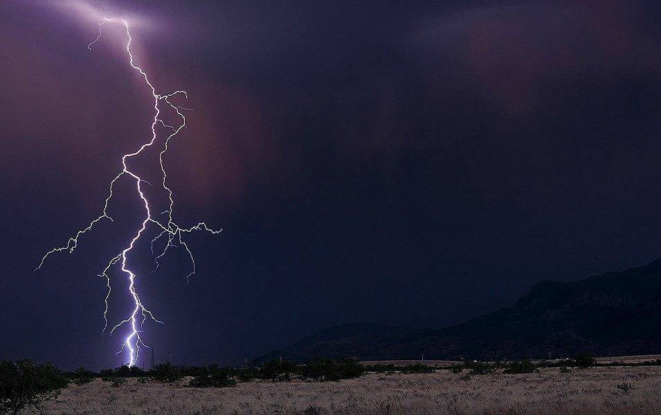 A big desert landscape is framed with a distant mountain range in the background. A single snake-like lightning bolt with multiple tentacles strikes the sparse landscape.