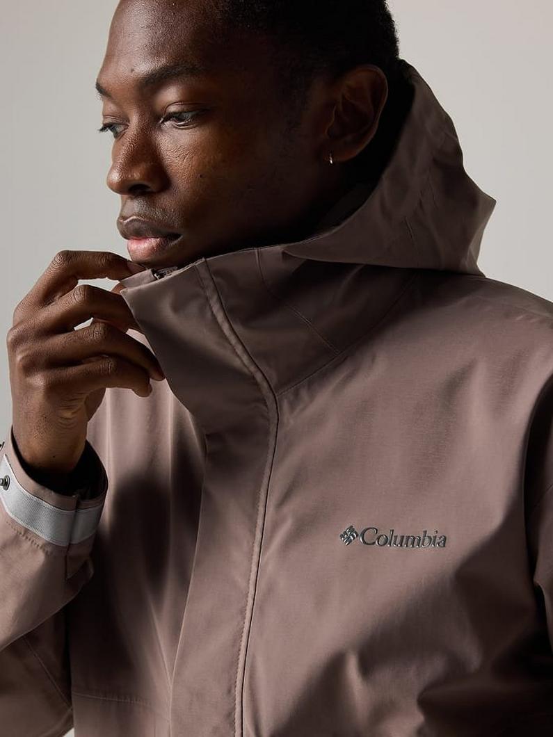 Model wearing a taupe zip-up jacket with high collar and small stud earring.