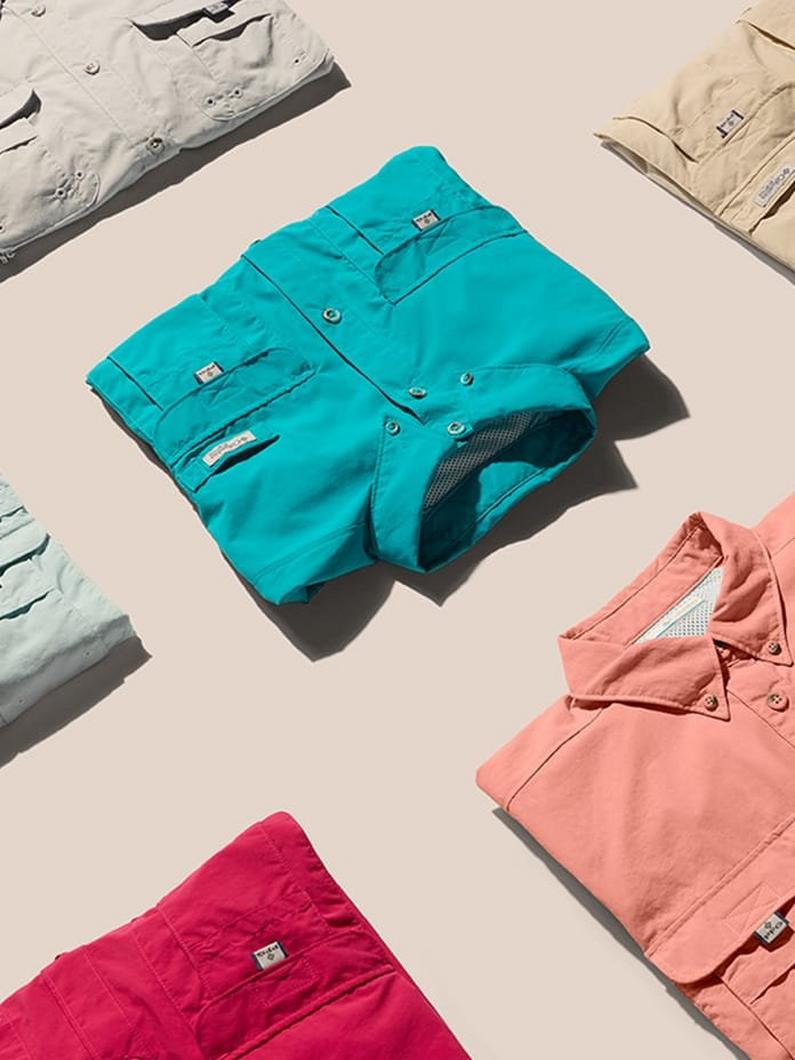 Folded utility shirts in turquoise, coral, magenta, gray, and tan with multiple pockets and button closures.