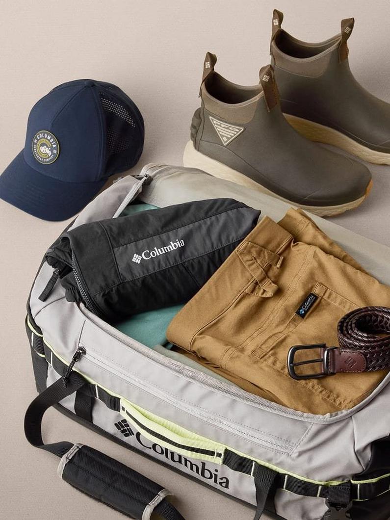 Open duffel bag packed with outdoor gear including navy cap, olive ankle boots, tan pants, and braided belt.