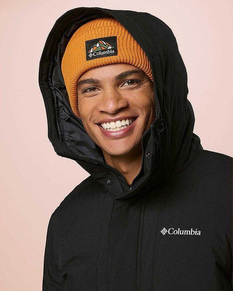 A man smiling wearing a green jacket and beanie.