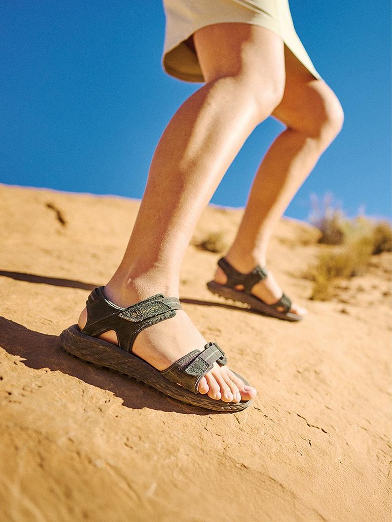 Person walking on desert sand wearing black sport sandals with adjustable straps.