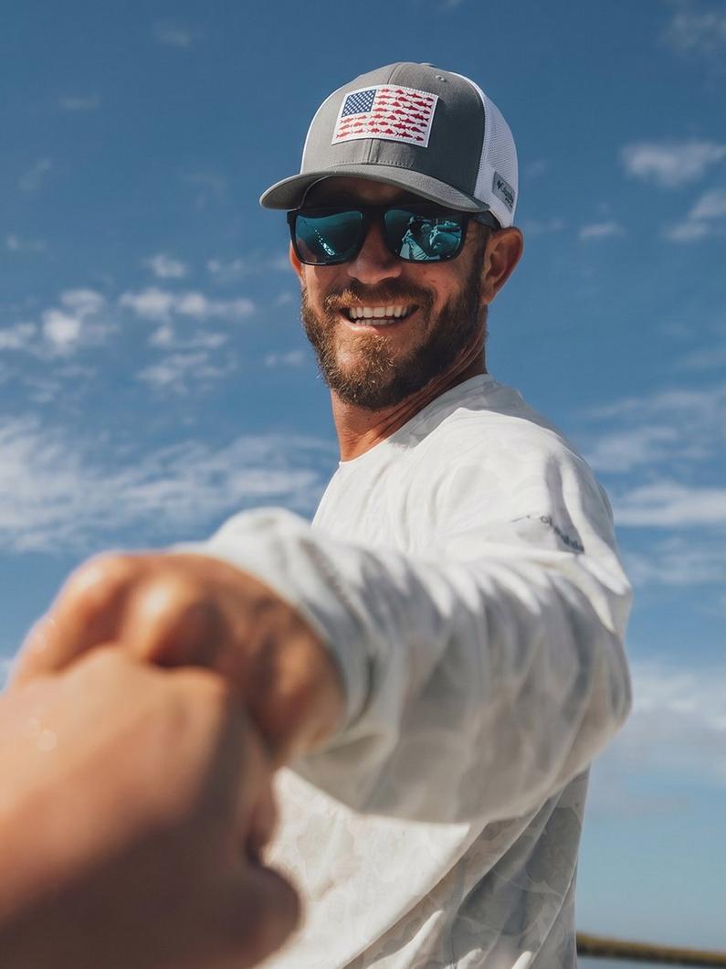 Man wearing sunglasses and American flag trucker cap smiling while fishing on water.