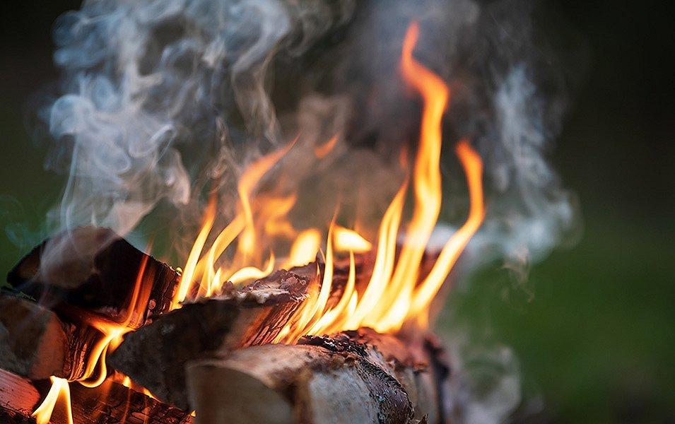 A campfire burns with wood split from a round log. The wood is placed so that there’s sufficient airflow between the logs. 
