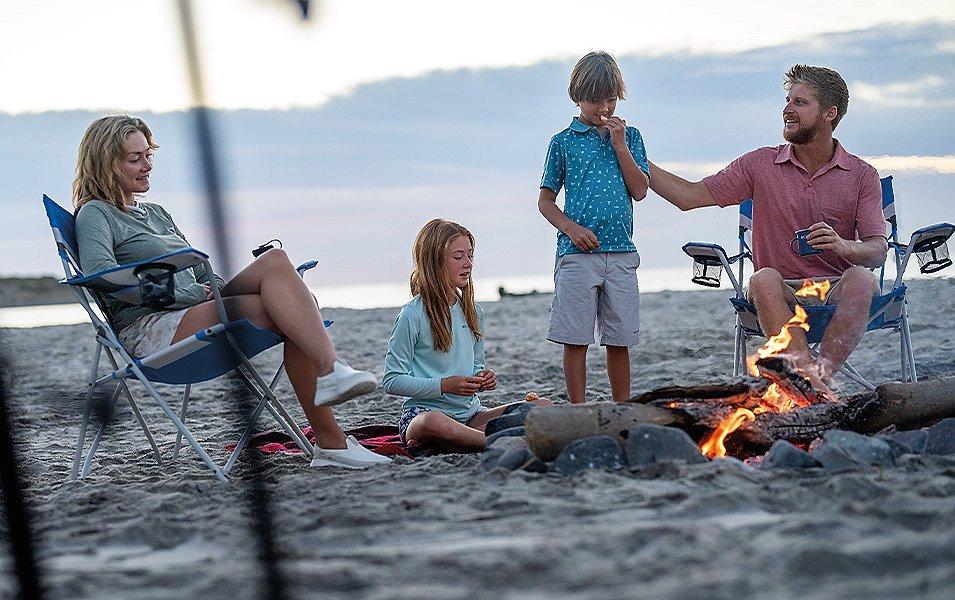 A family of four is sitting around a cozy campfire on a sandy beach.  